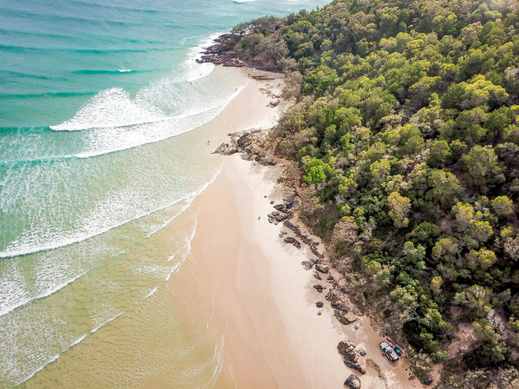 Stunning aerial view of Cooloola Beach in Queensland, Australia, with lush greenery and clear ocean waves.